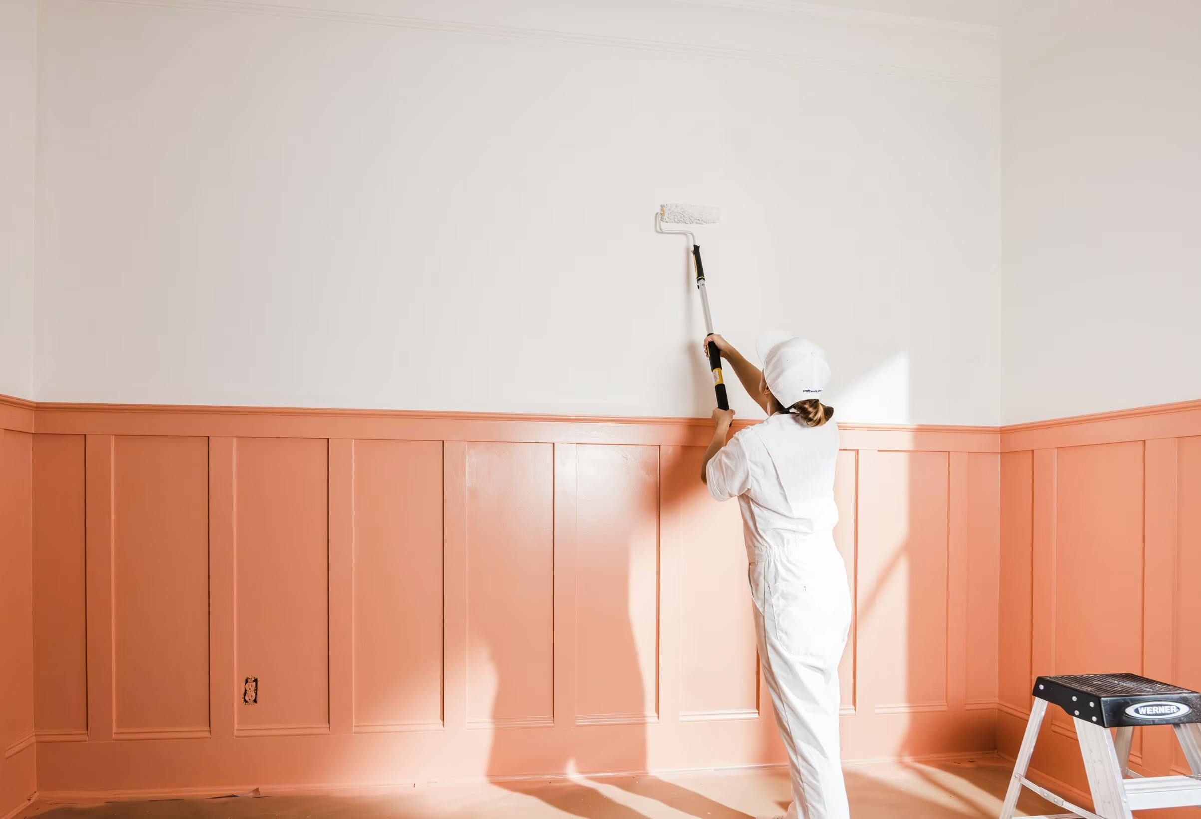 Craftwork painter painting a white wall with pink trim.
